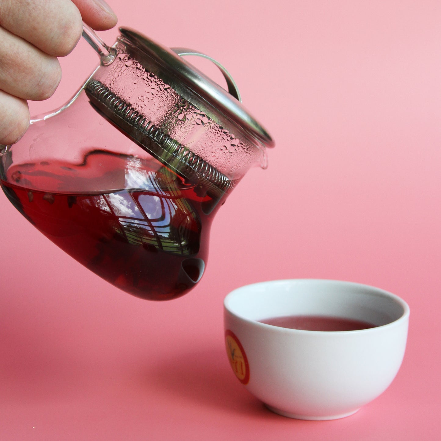 Hand pouring Royal Fruits infusion from glass tea pot into white tea bowl